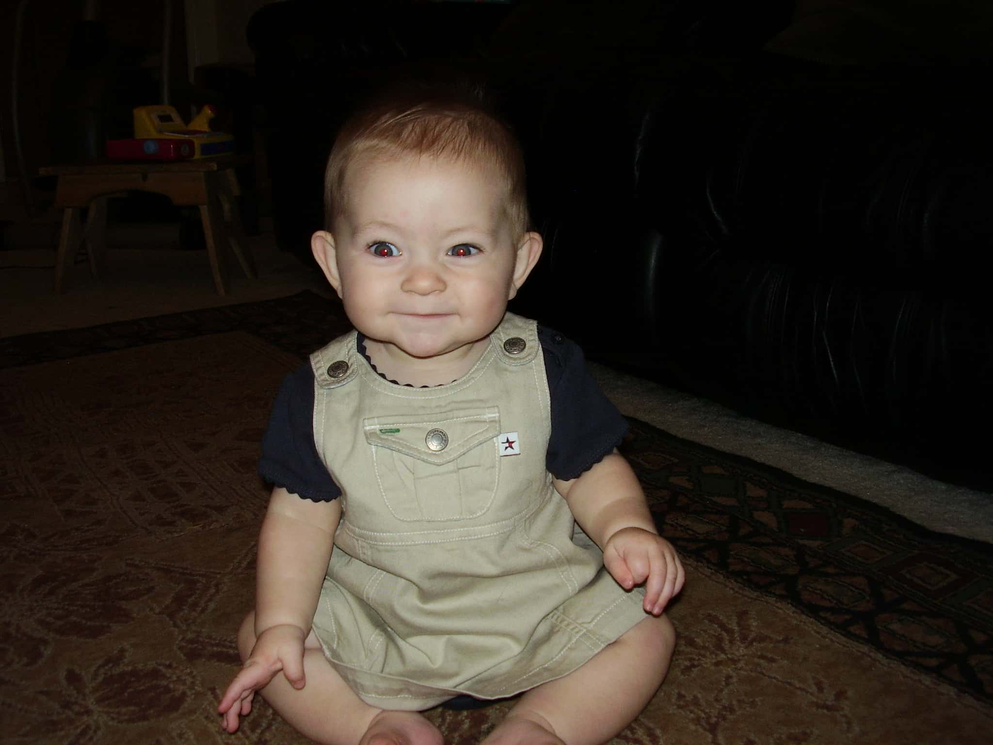 Smiling baby girl sitting on the floor in overalls