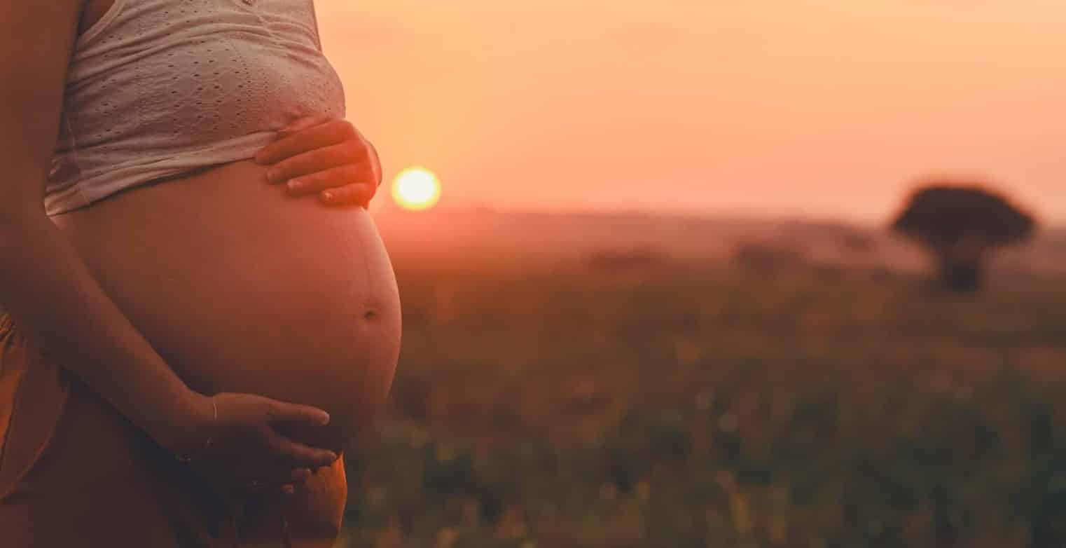 Pregnant woman holding belly in golden sunset field