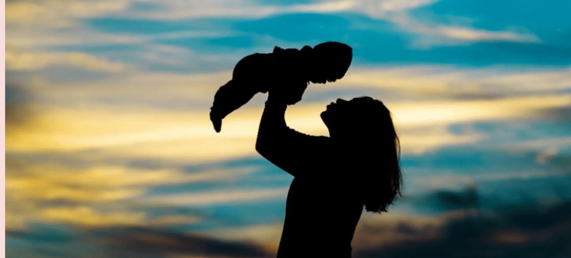 Mother lifting baby silhouette against colorful sunset sk